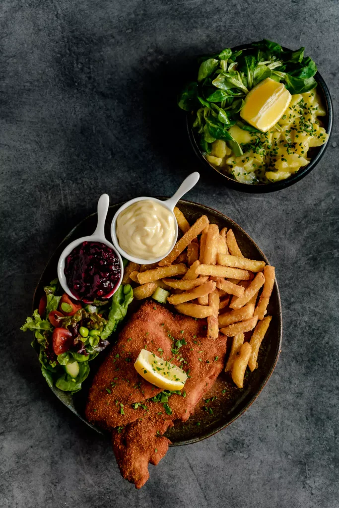 Schnitzel mit pommes, salat, preiselbeere und mayo, auf schwarzem Hintergrund